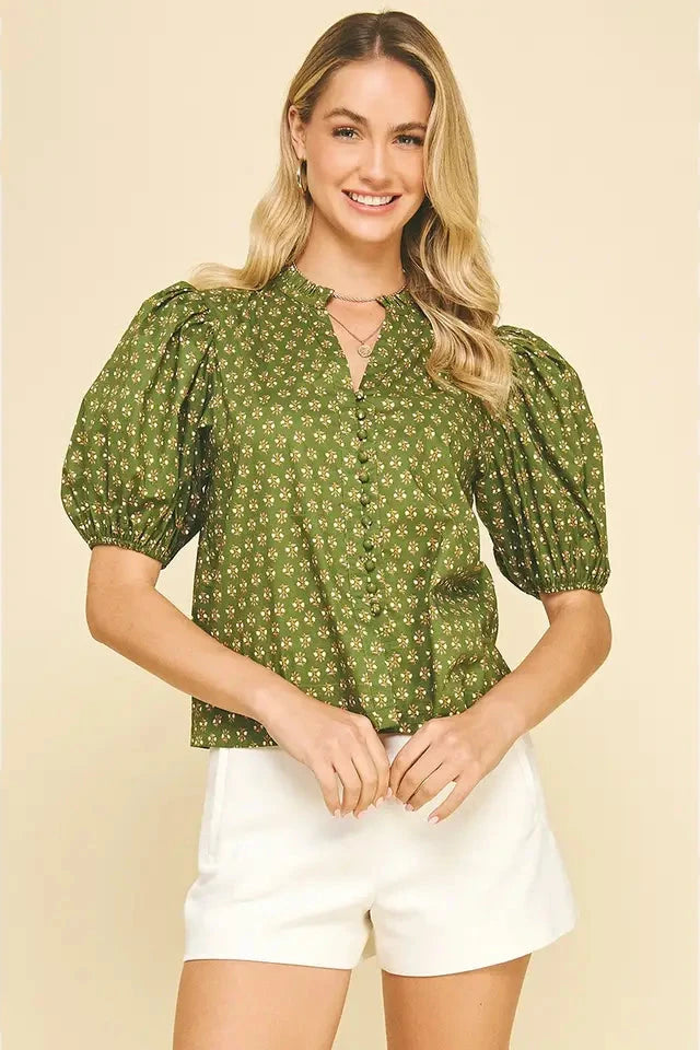 Woman wearing a green patterned blouse and white shorts on a beige background