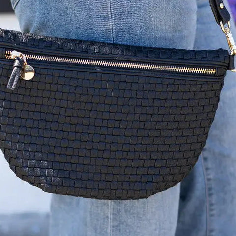 Black woven handbag with gold zipper and accents worn by a person in jeans.