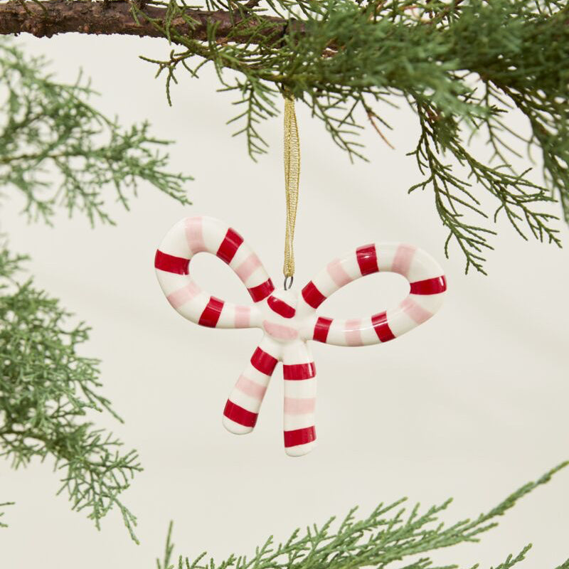 Candy cane ornament hanging on a Christmas tree branch with a light background