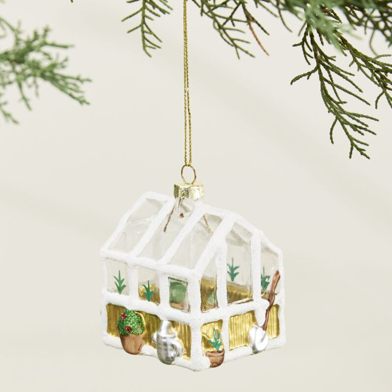 Decorative glass house ornament hanging on a tree branch with a light background