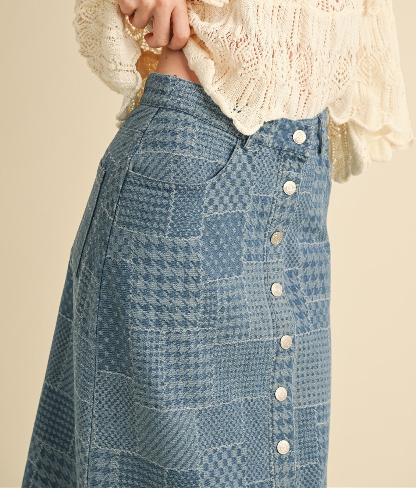 Person wearing a beige lace top and blue patterned skirt with white buttons.
