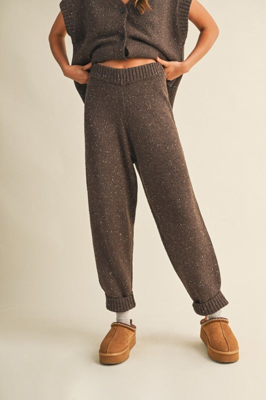 Person wearing brown knitted pants and a matching vest on a beige background