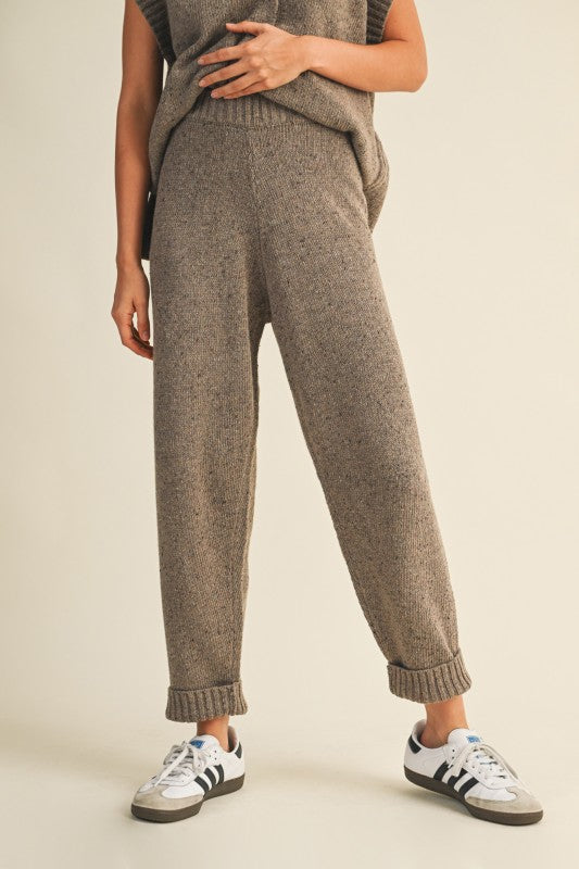 Person wearing brown knit pants and white sneakers on a beige background