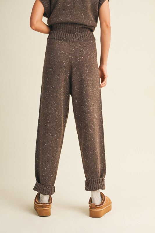 Person wearing brown knitted pants and a matching top on a beige background