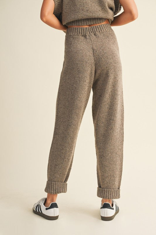 Person wearing brown knitted pants on a beige background