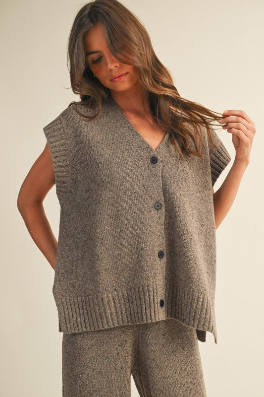 Woman wearing a brown knitted vest over a matching top and pants against a plain background