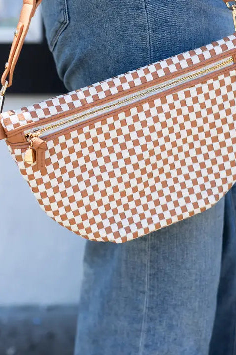 Checkered handbag with brown and white pattern held by a person wearing blue jeans.