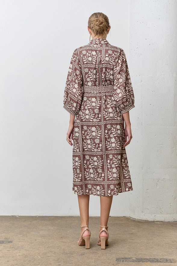 Woman wearing a patterned dress standing against a white wall.