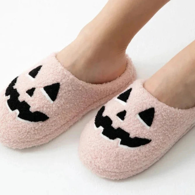 Pink slippers with black jack-o'-lantern faces worn by a person on a white background