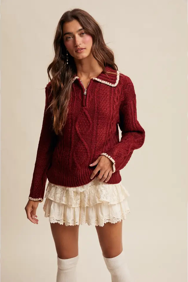 Woman wearing a red sweater with white trim and a white skirt on a beige background
