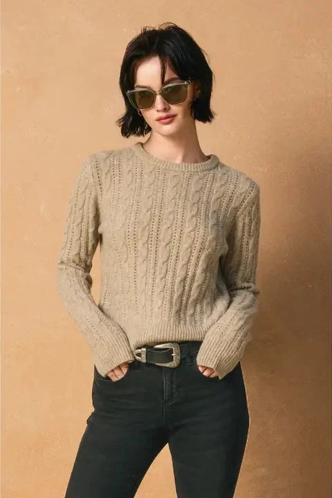 Woman wearing a beige cable knit sweater and sunglasses against a beige background