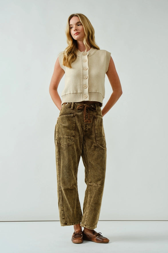 Woman wearing a sleeveless beige top and brown pants against a white background
