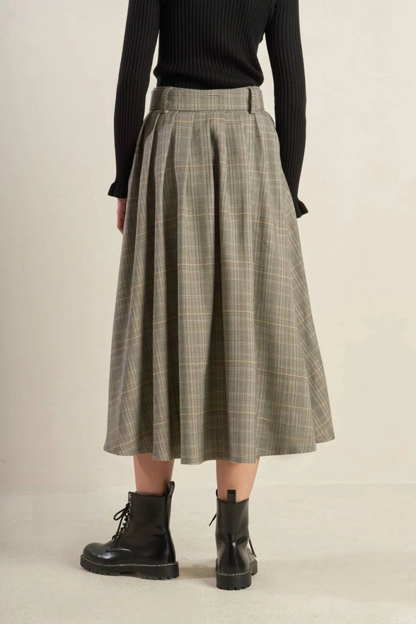 Person wearing a plaid skirt and black boots on a beige background