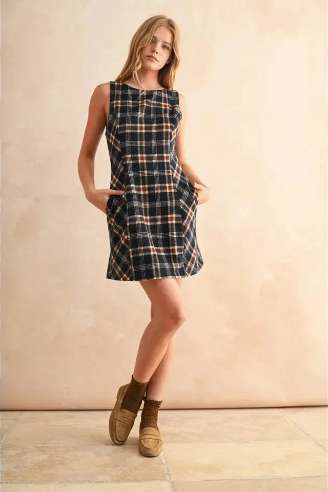 Woman wearing a plaid dress with brown shoes against a beige background