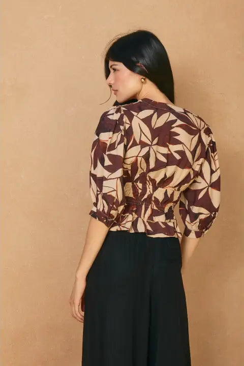 Woman wearing a patterned top and black pants against a beige background