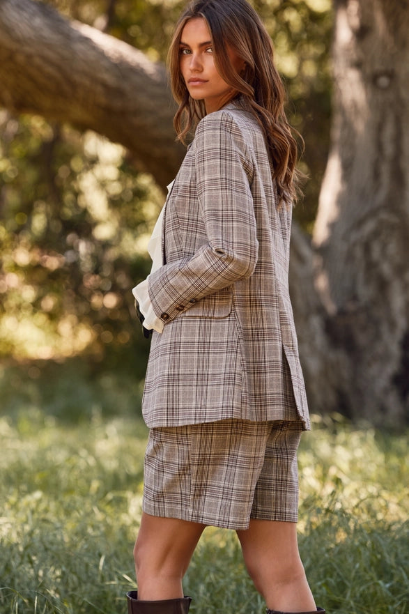 Woman wearing a plaid suit standing in a natural setting with trees and grass.