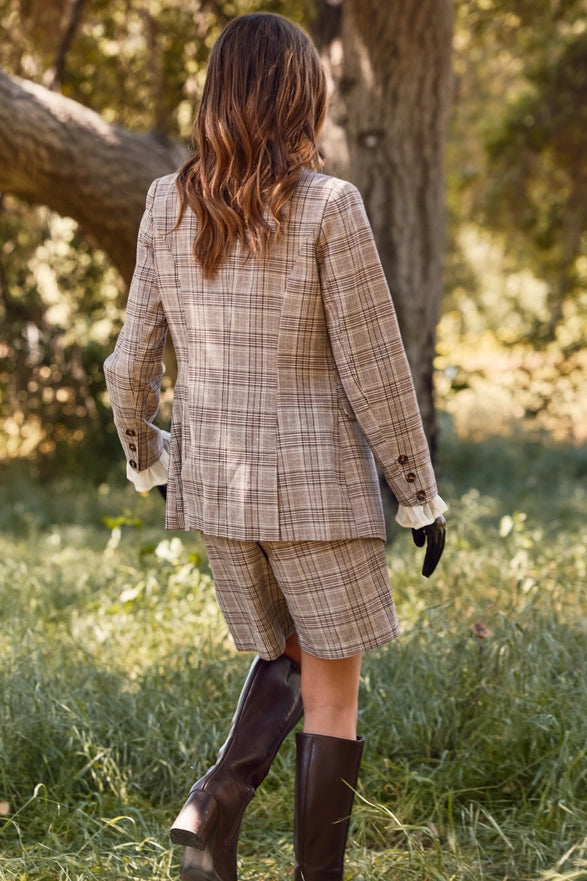 Person wearing a plaid suit walking through a grassy field with trees in the background
