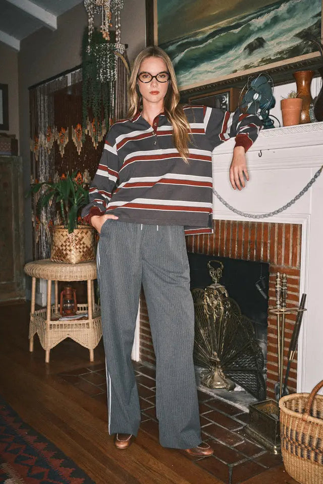 Woman in a striped shirt and gray pants standing in a room with a fireplace and decorative items.