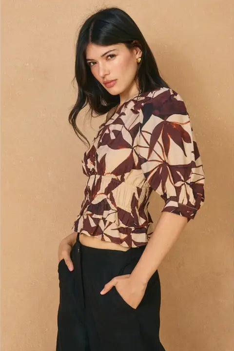 Woman wearing a patterned top and black pants against a beige background