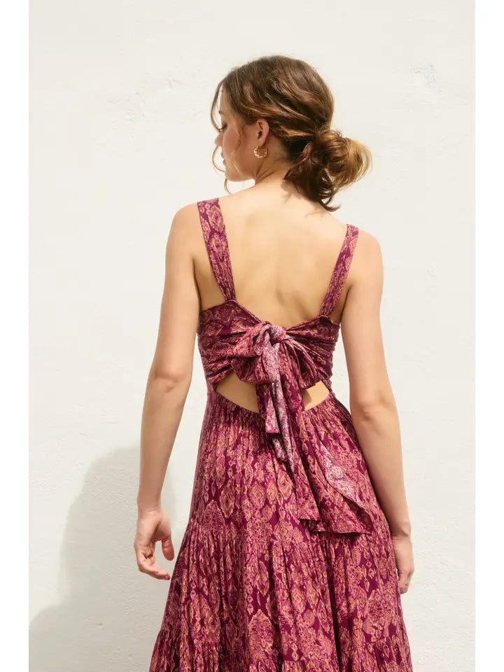 Woman wearing a pink floral dress with a tie-back detail on a white background