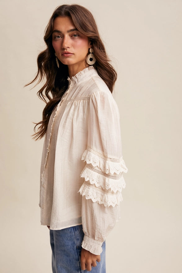 Woman wearing a beige blouse with lace details on a plain background