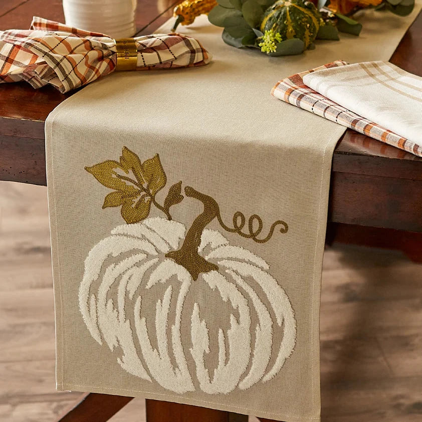 Table runner with pumpkin design on a wooden table with fall decorations.