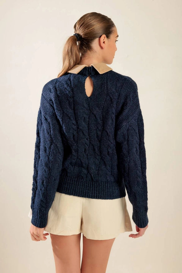 Person wearing a navy blue cable knit sweater with a cut-out back design on a beige background