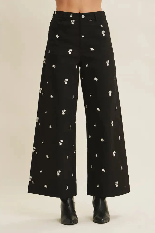Black wide-leg pants with white floral pattern on a beige background