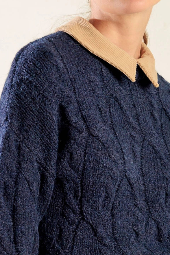 Navy blue cable knit sweater with a beige collar on a neutral background