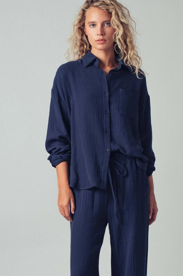 Woman wearing a navy blue shirt and pants on a plain background