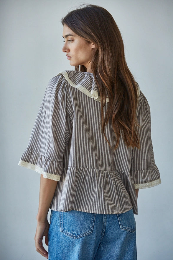 Woman wearing a striped shirt with ruffled sleeves and blue jeans against a plain background