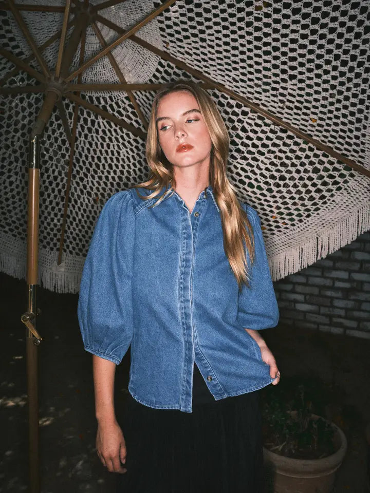 Woman wearing a blue denim shirt standing under a decorative umbrella with a patterned roof.