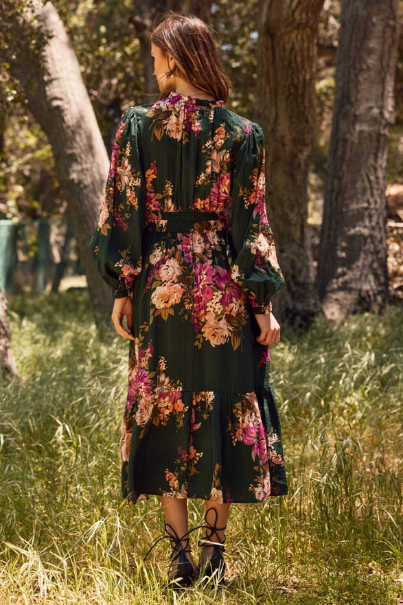 Woman in a floral dress standing in a grassy area with trees.