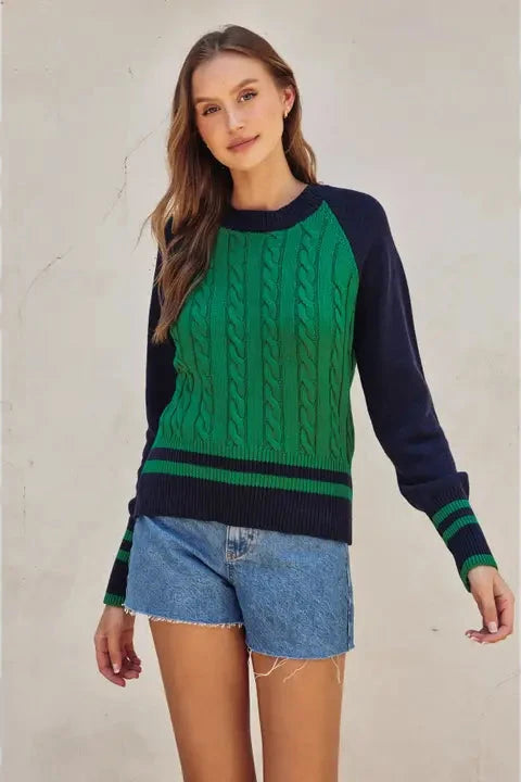 Woman wearing a green and navy sweater with denim shorts on a neutral background