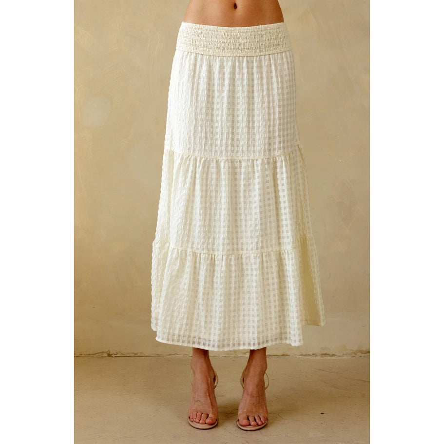 A midi-length tiered skirt with a smocked waistband, designed with a subtle checkered pattern in a beige color.