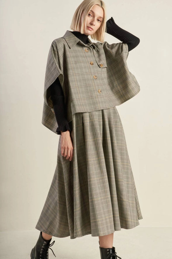 Woman wearing a plaid dress with a cape over a plain background