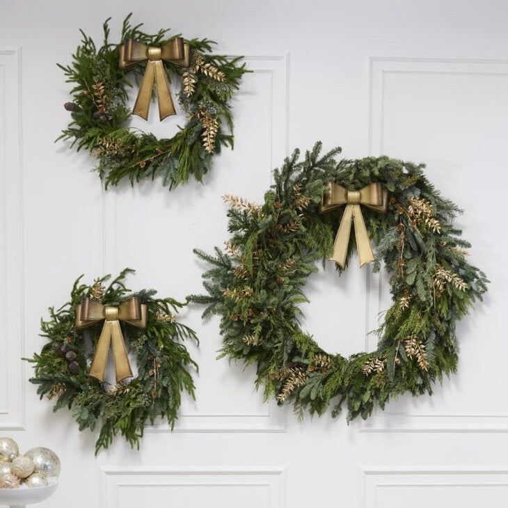 Three green wreaths with gold ribbons hanging on a white wall above a sofa.