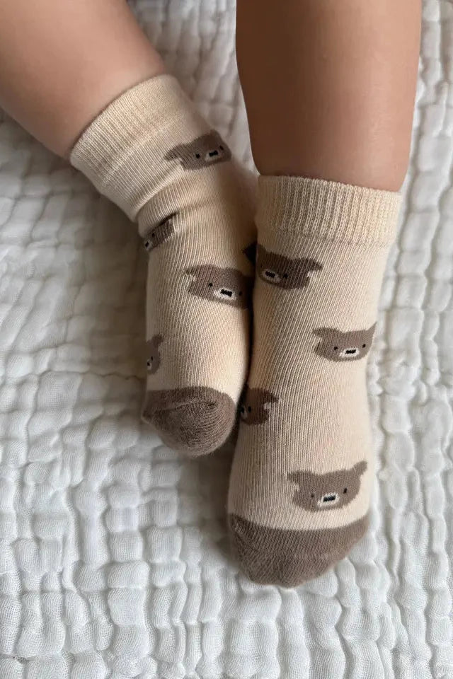 Beige socks with bear patterns worn by a person on a textured white surface
