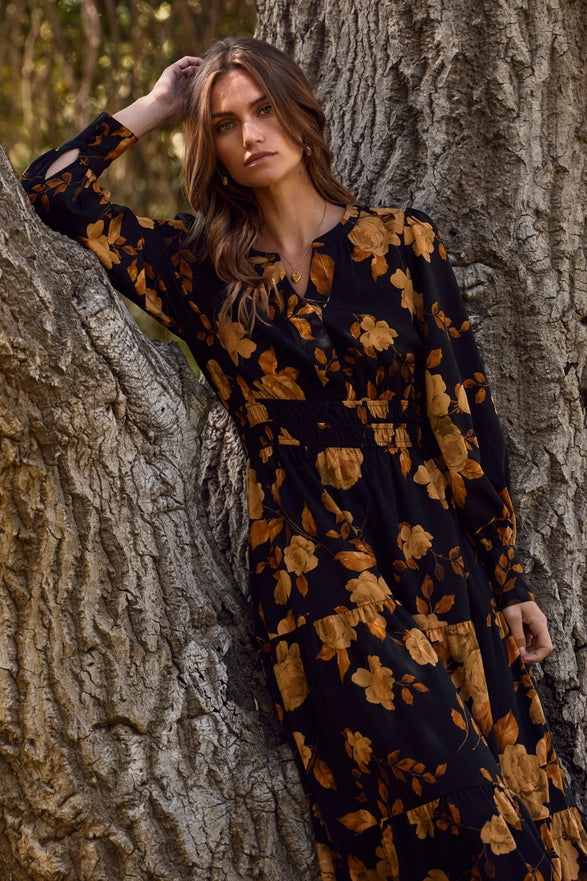 Woman in a floral dress leaning against a tree