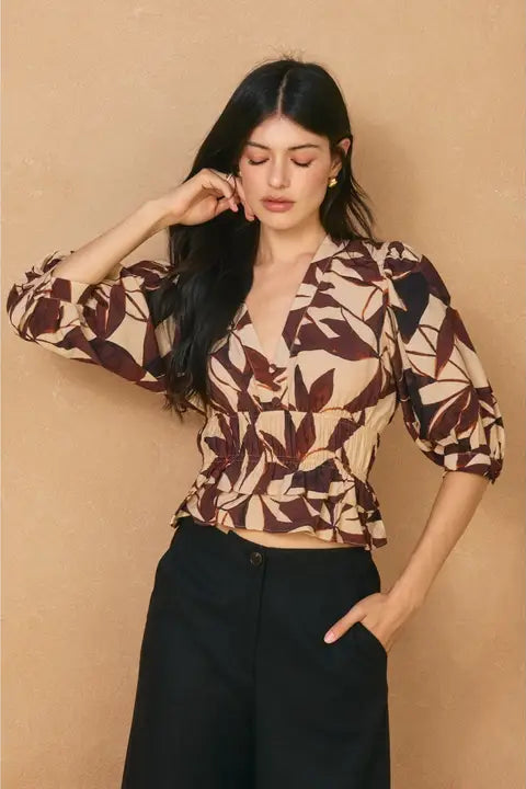 Woman wearing a patterned top and black pants against a beige background