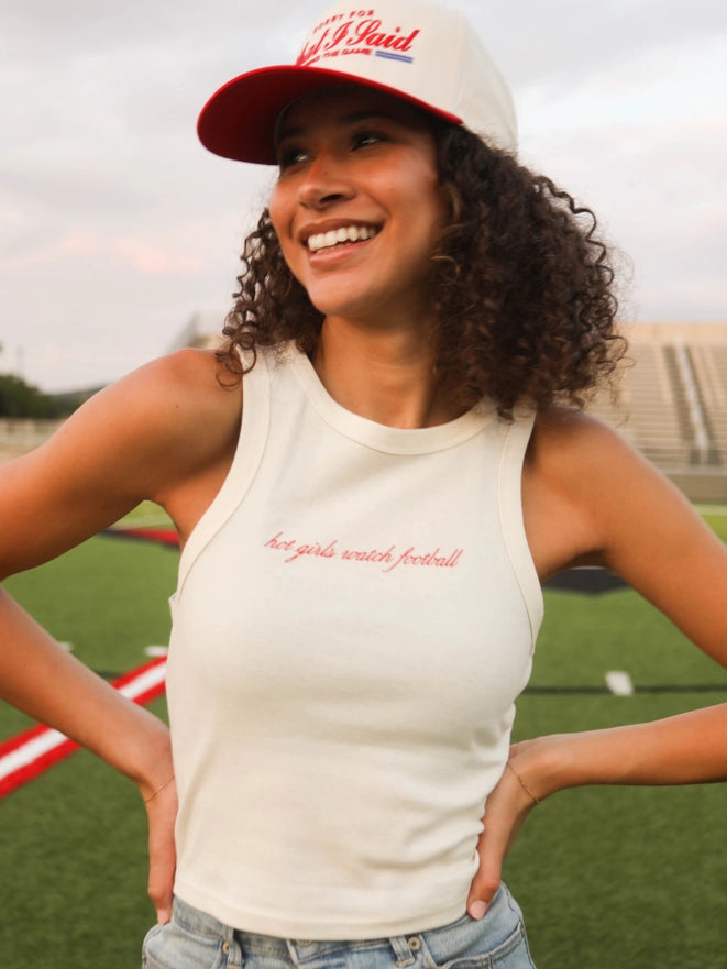 Woman wearing a white tank top with text and a cap on a sports field.