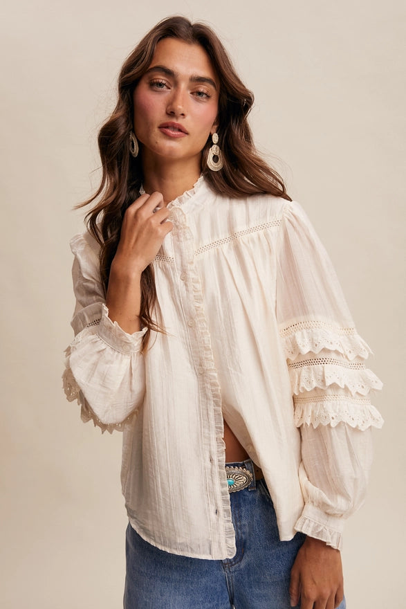 Woman wearing a white lace blouse with long sleeves and blue jeans on a beige background