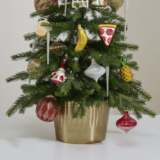 Small decorated Christmas tree with various ornaments in a gold pot on a white surface.