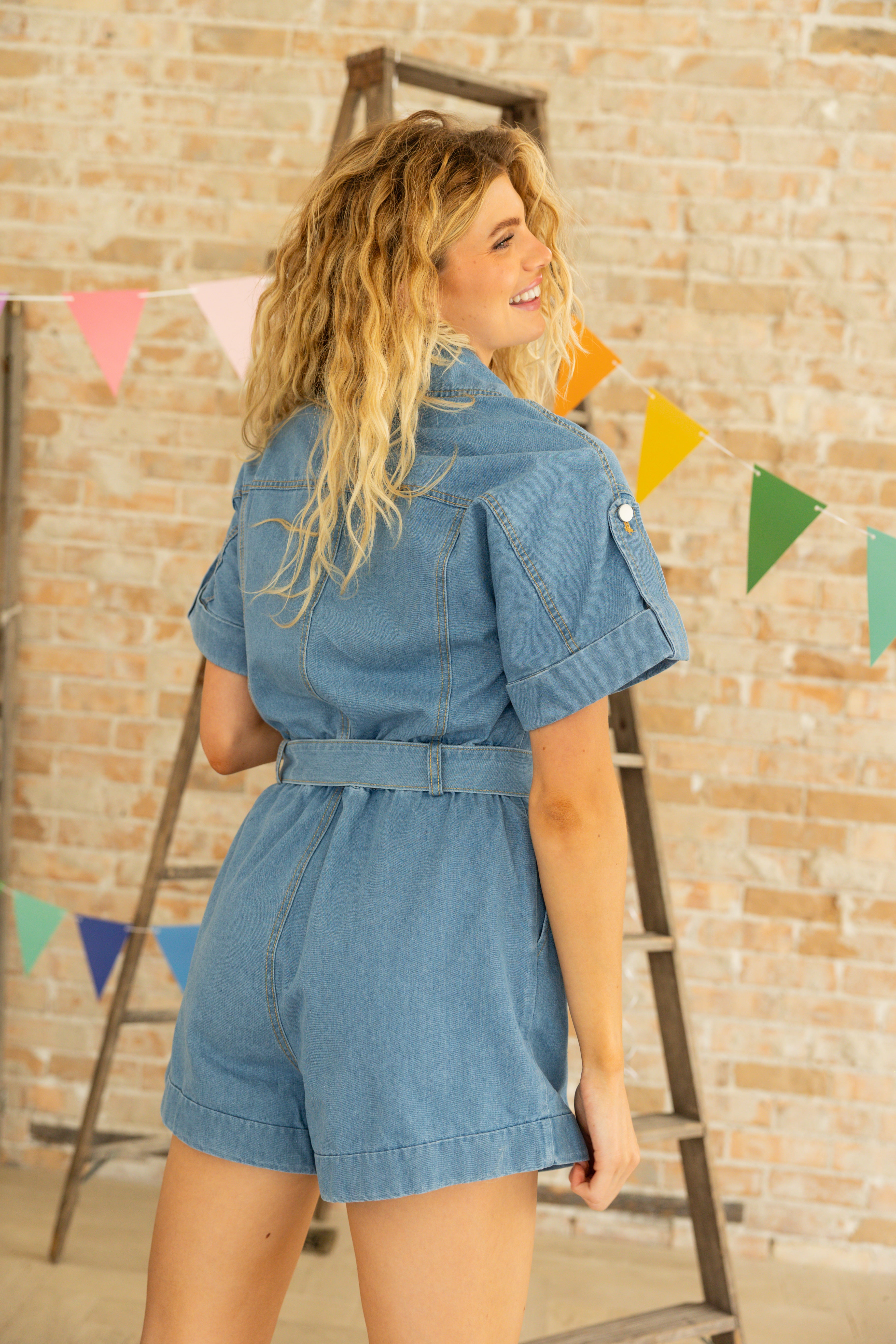 Model is wearing a short sleeve and shorts denim romper with belt.