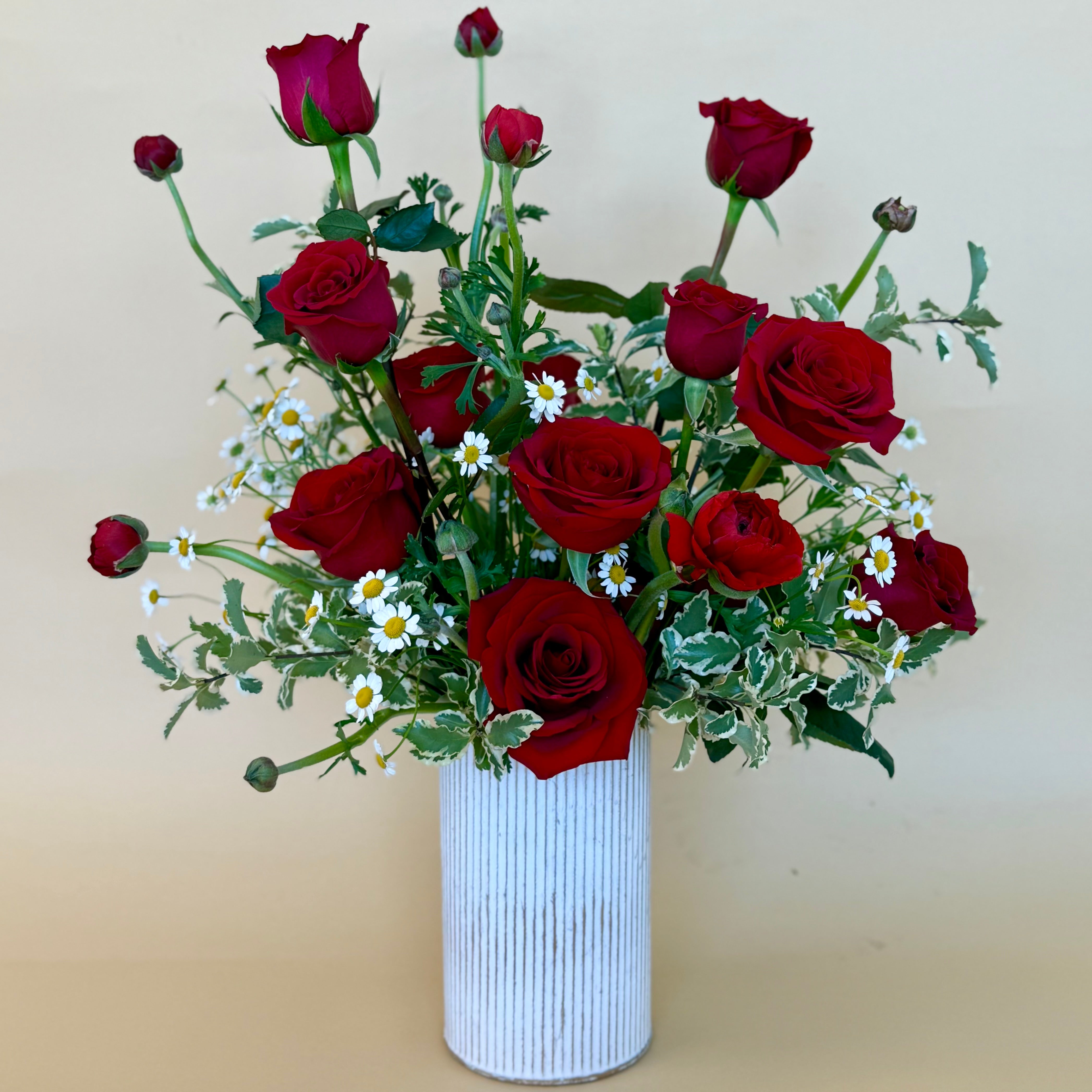 Vase arrangement of red roses with daisies and greenery.