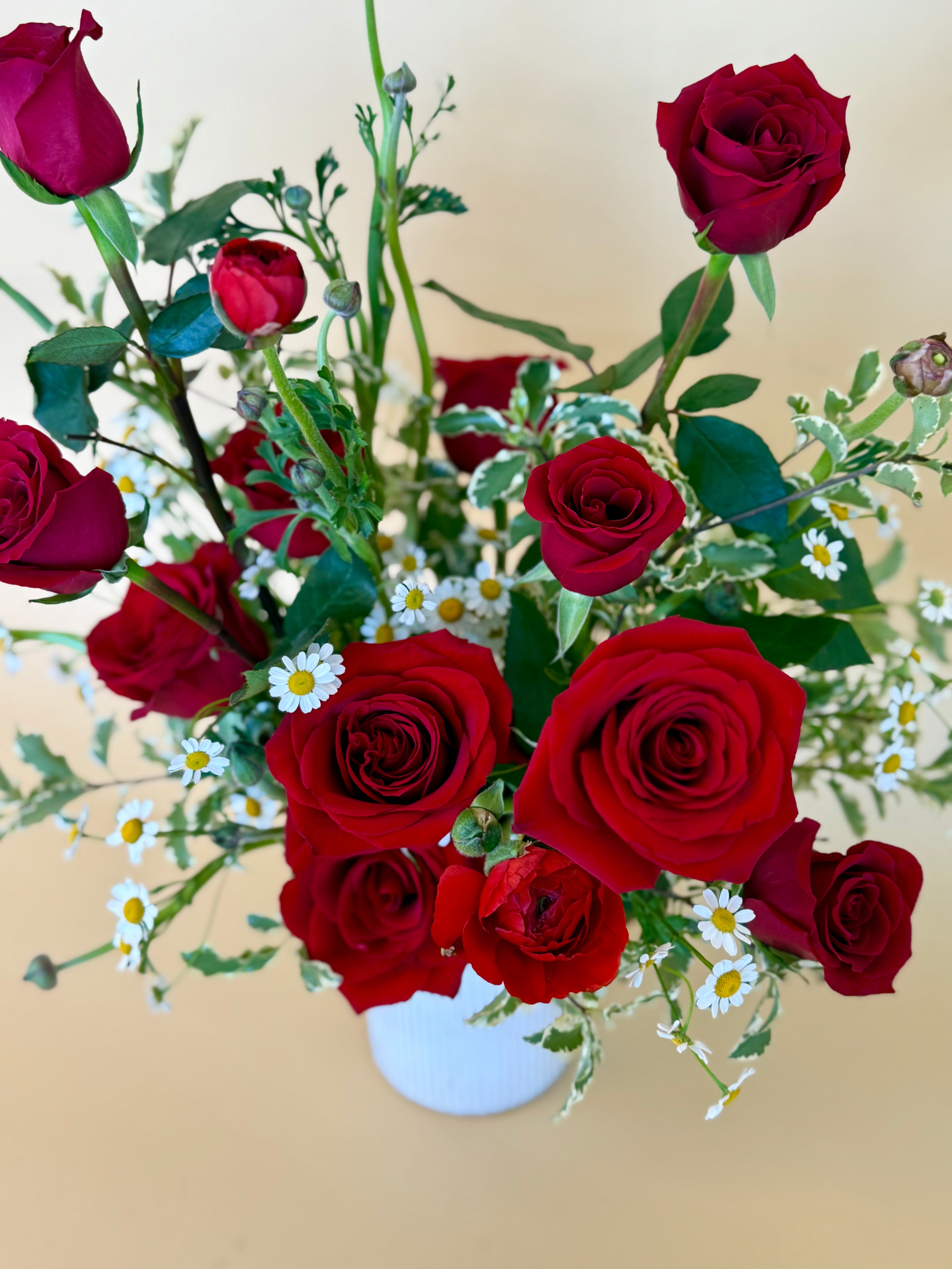 Vase arrangement of red roses with daisies and greenery.