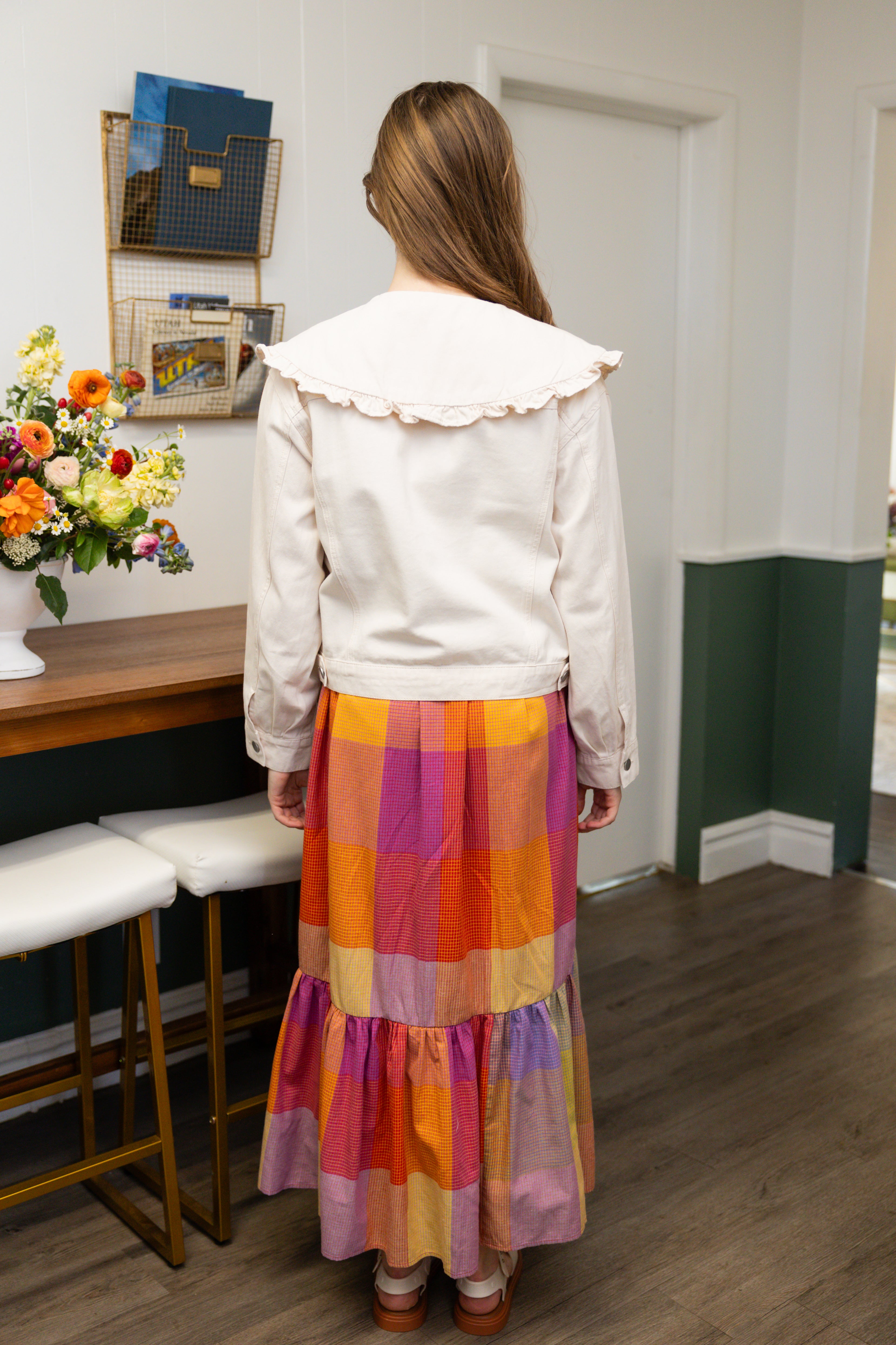 Model is wearing ruffle collar white denim jacket and colorful dress.