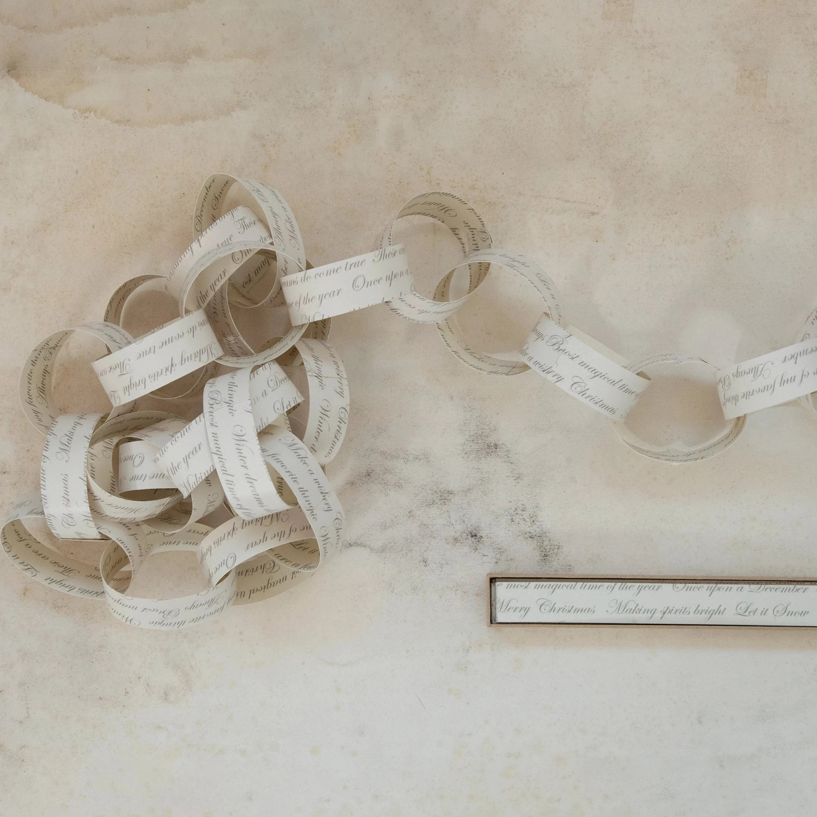 Decorative paper chain on a textured beige surface with a small plaque.