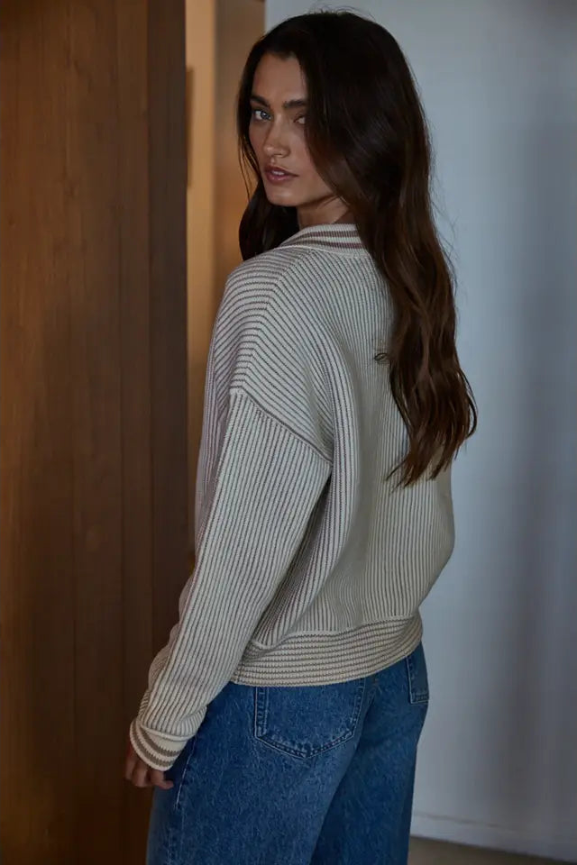 Woman wearing a striped sweater and blue jeans standing against a wooden door.