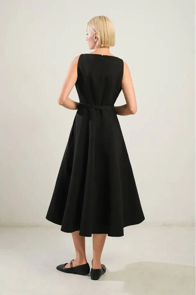 Woman wearing a black sleeveless dress with a belt on a plain background